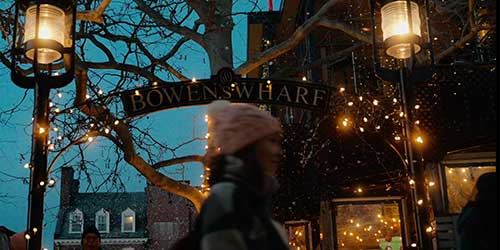 Entrance to Bowen’s Wharf in Newport decorated with glowing lights and waterfront shopping atmosphere at dusk.