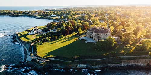 Aerial view of Newport’s Cliff Walk winding along the rocky coastline beside historic seaside mansions.