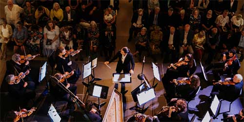Live orchestra performance by Newport Classical featuring musicians and audience gathered in an intimate concert setting.