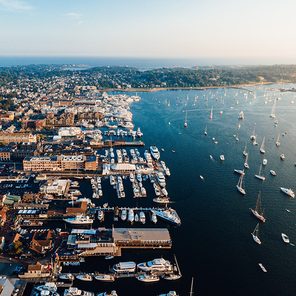 Aerial view of Newport Harbor in Rhode Island filled with sailboats and marinas along the waterfront with the coastal city stretching inland.